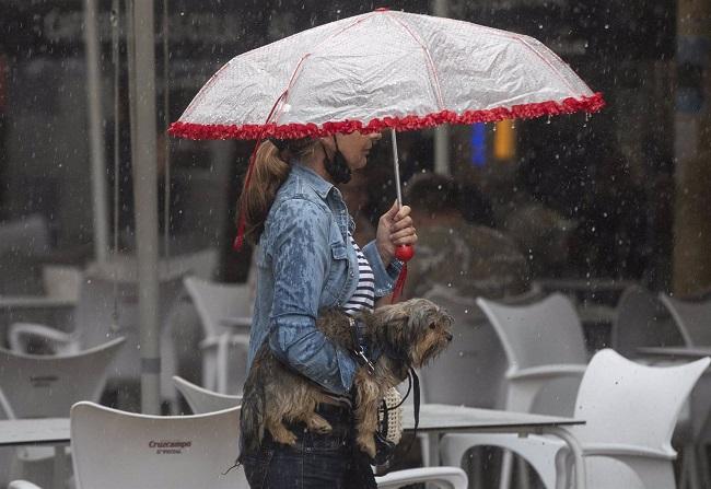 Una mujer lleva a su perro en brazos bajo una tormenta, en una imagen de archivo. 