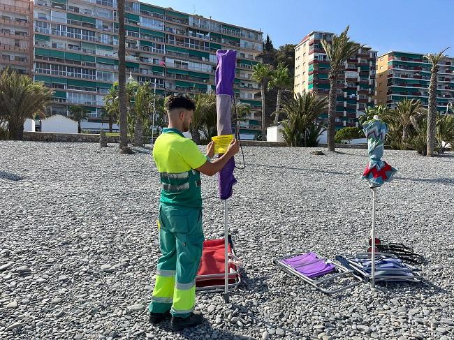 Un operario coloca una pegatina en una sombrilla, en la Playa de Velilla, advirtiendo de que será retirada. 