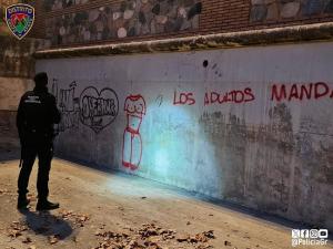 Un agente, frente a las pintadas hechas en el muro del cauce del río que da a los jardines del Salón.