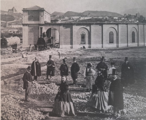 Un grupo de personas posa, hacia 1864-6, en la estación de Andaluces delante de la rotonda de locomotoras, con Granada al fondo. 